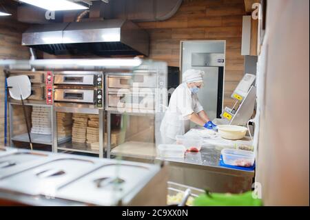 Pizzahersteller in Schutzmaske in der Pizzeria arbeiten. Stockfoto