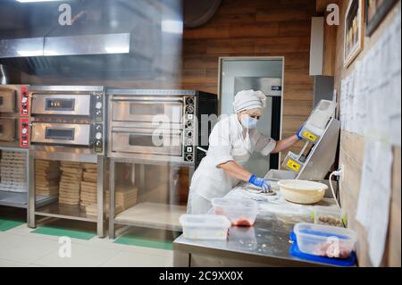 Pizzahersteller in Schutzmaske in der Pizzeria arbeiten. Stockfoto