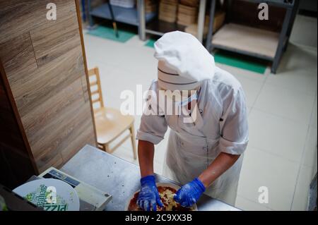 Pizzahersteller in Schutzmaske in der Pizzeria arbeiten. Stockfoto