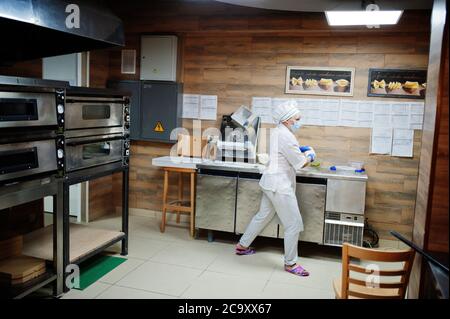 Pizzahersteller in Schutzmaske in der Pizzeria arbeiten. Stockfoto
