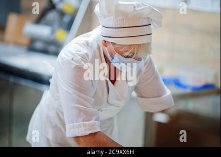 Pizzahersteller in Schutzmaske in der Pizzeria arbeiten. Stockfoto