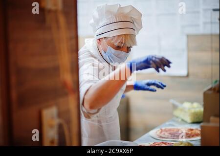 Pizzahersteller in Schutzmaske in der Pizzeria arbeiten. Stockfoto