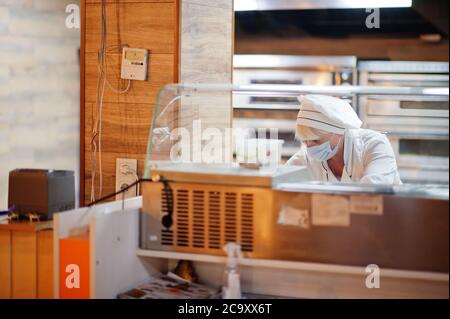 Pizzahersteller in Schutzmaske in der Pizzeria arbeiten. Stockfoto