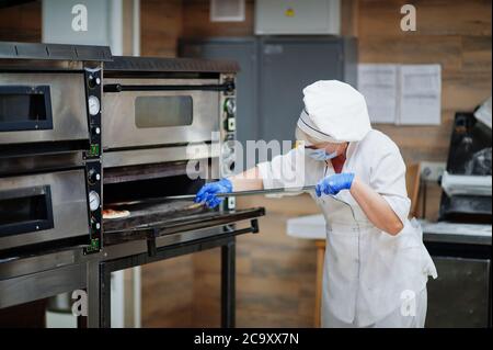 Pizzahersteller in Schutzmaske in der Pizzeria arbeiten. Stockfoto