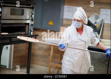 Pizzahersteller in Schutzmaske in der Pizzeria arbeiten. Stockfoto