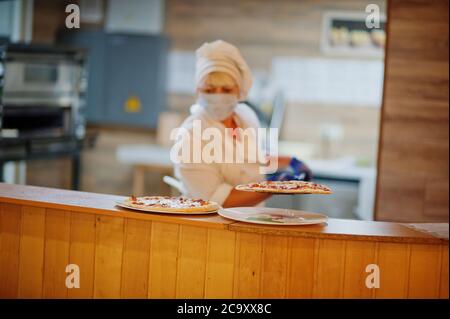 Pizzahersteller in Schutzmaske in der Pizzeria arbeiten. Stockfoto