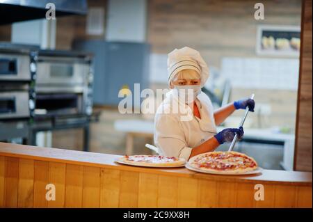 Pizzahersteller in Schutzmaske in der Pizzeria arbeiten. Stockfoto