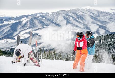 Horizontale Schnappschüsse Gruppe von Freunden in lebendigen Wintersport-Anzüge Spaß im Schnee in den Bergen. Skistöcke und Skier stecken im Schnee, die Leute spielen Schneebälle. Winter-Entertainment-Konzept Stockfoto