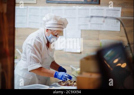 Pizzahersteller in Schutzmaske in der Pizzeria arbeiten. Stockfoto