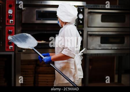 Pizzahersteller in Schutzmaske in der Pizzeria arbeiten. Stockfoto