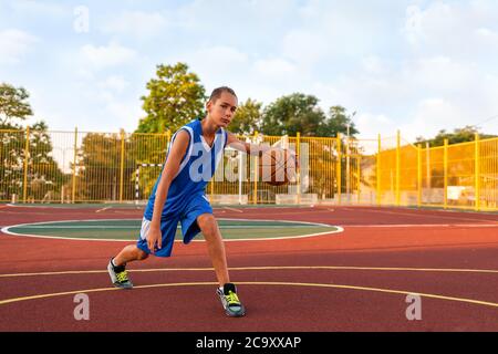 Basketball. Ein Teenager in blauer Sportkleidung spielt Basketball. Im Hintergrund ist ein Sportplatz. Konzept der Sportspiele. Stockfoto