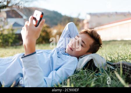 Handy und Internet. Ein Teenager liegt im Park auf dem Rasen und schaut sich ein Video auf einem Smartphone an. Stockfoto