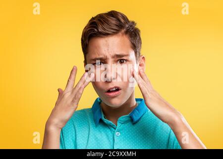 Kosmetologie, Dermatologie und Akne. Ein kaukasischer Teenager in einem blauen T-Shirt ist über das Auftreten von Akne verärgert. Gelber Hintergrund. Speicherplatz kopieren. Stockfoto