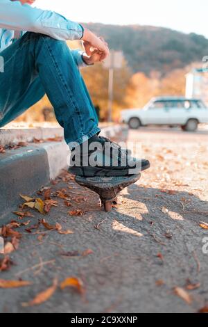 Ein Teenager sitzt auf einer Stufe mit seinen Füßen auf einem Skateboard. Straße im Hintergrund. Vertikal. Stockfoto