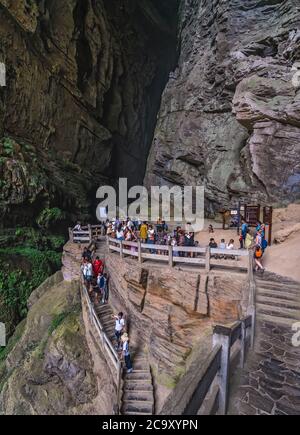 Wulong, China - August 2019 : Touristen klettern Schritte in einer atemberaubenden massiven Höhle in einer Schlucht zwischen Karstlandschaft des Wulong National Park Stockfoto