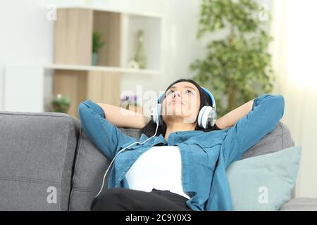 Entspannte Frau, die Musik hört, mit Kopfhörern, die auf einem Sofa im Wohnzimmer zu Hause sitzen Stockfoto
