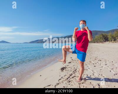 Junge Muskelmann in medizinische Maske führen Outdoor-Workouts im Park in der Nähe von Meer während der zweiten Welle Coronavirus Covid 19 Pandemie Quarantäne. Tritt Stockfoto