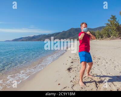 Junge Muskelmann in medizinische Maske führen Outdoor-Workouts im Park in der Nähe von Meer während der zweiten Welle Coronavirus Covid 19 Pandemie Quarantäne. Tritt Stockfoto