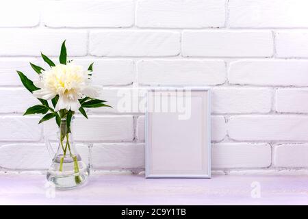 Weißer kleiner Rahmen Mockup mit cremefarbenem Pfingstrosen in der Glas-Krug-Vase. Leerer Rahmen für Präsentationsgrafiken. Schablonenrahmen für moderne Kunst Stockfoto