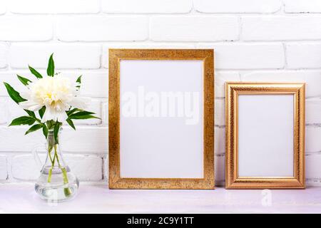 Zwei goldene Rahmen Mockup mit weißem Pfingstrose in der Glas Krug Vase. Leerer Posterrahmen für Präsentationsgestaltung. Schablonenrahmen für modernes A Stockfoto