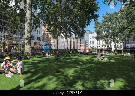 Im Sommer sitzen Menschen in Leicester Square Gardens, öffentliche Grünflächen in Soho, London, England, Großbritannien Stockfoto