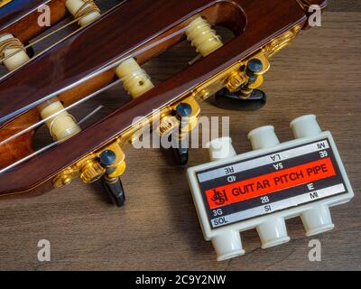 Kopfplatte / Peghead und Tuner einer klassischen Gitarre, neben einem Jahrzehnte alten Kunststoff-Pitch-Rohr (durchgeblasen, um die Tonhöhe für jede Saite zu hören). Stockfoto