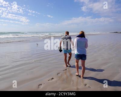 Junges Paar in Sommerkleidung auf menschenleeren, weißen Sandstrand zu Fuß Stockfoto