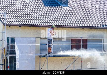 Mann, der die Front und das Dach eines Hauses putzt Stockfoto