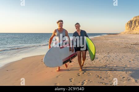 Reifes Paar mit Surfbrettern am schönen Strand, das Paradies und aktiven Lebensstil genießen. Attraktiv fit Mann und Frau Surfen und Spaß haben. In Trave Stockfoto