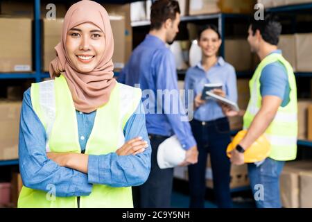 Portrait of Islam muslimische Lagerarbeiterin kreuzte den Arm mit ihren Kollegen, die sich im Lager-Distributionszentrum treffen. Für Geschäftsreisende wa Stockfoto