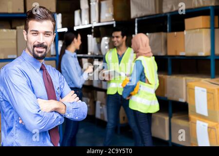 Porträt des weißen kaukasischen Lagerhausbesitzers gekreuzt Arm mit seinem Arbeiter Meeting Hintergrund in Lager-Distributionszentrum-Umgebung. Geschäftswelt Stockfoto