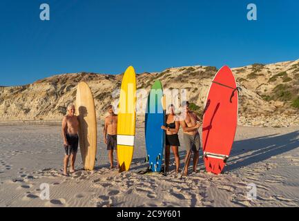 Gruppe von älteren Surfern, Frauen und Männer, halten ihre bunten Surfbretter am abgelegenen Strand. Ältere Freunde im Ruhestand genießen Surfen und im Freien am lebendigsten Stockfoto