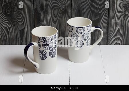 Zwei Keramikbecher auf einer weißen Oberfläche. Vor einem Hintergrund von Kiefernbrettern schwarz lackiert. Stockfoto