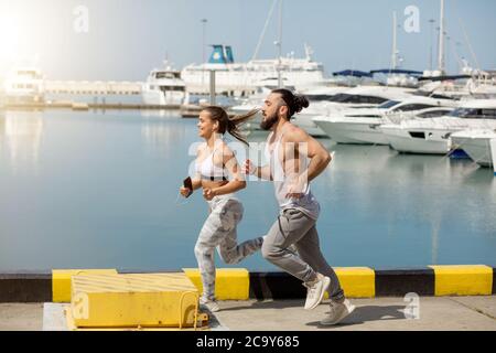 Zwei Läufer sprintete im Freien - Männliche und weibliche Athleten Training am Wasser oder Pier mit Motorbooten und Yachten. Gesunde Lebensweise. Sport und Freizeit Stockfoto