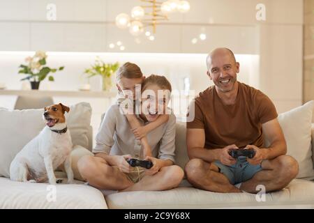 Niedliche warm-getönten Porträt von glücklichen modernen Familie spielen Videospiele zusammen, während sitzen auf der Couch in gemütlichen Innenraum, lächelnd reifen Mann genießen Stockfoto