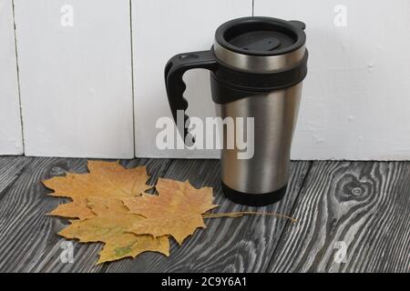 Thermo Becher auf einer Pine Board Oberfläche. In der Nähe sind getrocknete Ahornblätter. Stockfoto