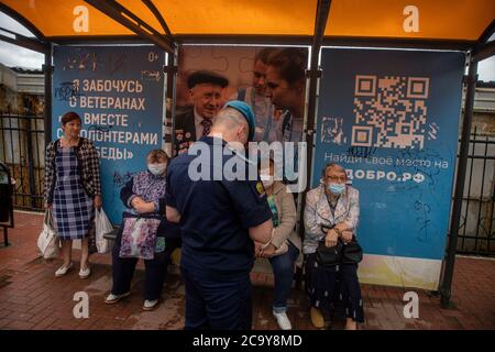 Rjasan, Russland. Am 2. August warten 2020 Menschen mit Schutzmasken an einer Bushaltestelle in der Stadt Rjasan auf die öffentlichen Verkehrsmittel. Auf dem linken Banner steht: "Ich kümmere mich um Veteranen zusammen mit den Helfern des Sieges" Stockfoto