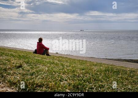 Harlingen,Niederlande,Juli,23,2020:Silhouette Rückseite der jungen Frau auf einem Deich mit Blick auf das Wattenmeer. Denken an Probleme während der Corona-Krise Stockfoto