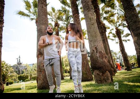 Portrait von schönen jungen Paar in Sport Outfit, die im Freien arbeiten am Morgen mit tropischen Palmen. Fitness Mädchen mit Kopfhörern ru Stockfoto