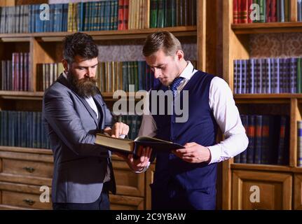 Intelligente Männer treffen sich in der Bibliothek. Intelligente Elite und wissenschaftliche Menschen Konzept. Herren-Anzug mit Vintage-Bücherregalen im Hintergrund. Professoren mit durchdachten Gesichtern lesen Buch in antikem Interieur. Stockfoto