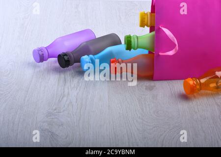 Energy Drinks Behälter mit verschiedenen Geschmacksrichtungen. Einkaufstasche mit bunten Getränken auf hölzernem grauem Hintergrund. Farbauswahl und Behälterkonzept. Set von Flaschen in verschiedenen Farben innerhalb rosa Paket Stockfoto