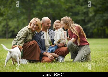 Full length Portrait of happy modern happy family with two daughters and PET Dog sitting on Green Grass Outdoor and joying time in Park together, copy space Stockfoto