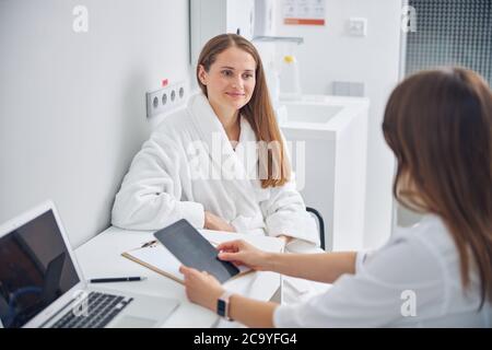 Lächelnde Dame in einem weißen Bademantel auf einem Stuhl sitzend Stockfoto