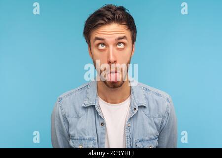 Porträt des Idiot Mann in Denim-Shirt machen dumm humorvollen Gesicht mit gekreuzten Augen und Zunge aus, zeigt komisch dumm hirnlosen Gesichtsausdruck. i Stockfoto