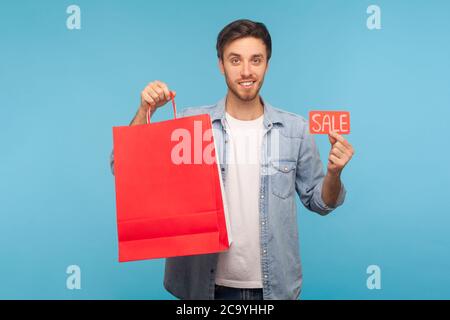 Portrait von fröhlich gut aussehend stilvolle Shopper Mann in Denim-Shirt Holding Verkauf Inschrift und Pakete mit Leerzeichen für inserieren Text, Rabatt i Stockfoto