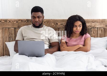Süchtig schwarzen Mann mit Laptop im Bett, Frau, die wütend Stockfoto