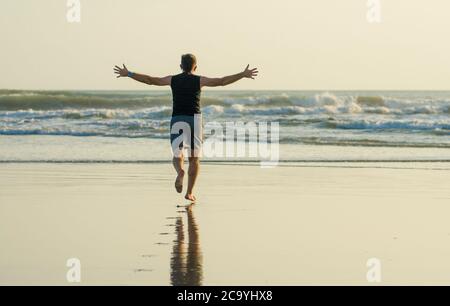 Silhouette eines Mannes, der die Arme öffnet, der nach dem Meer läuft und sich frei und glücklich fühlt nach dem covid19 Lockdown Alptraum Stockfoto