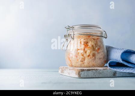 Glas mit Metallclip voll hausgemachtem Sauerkraut mit Karotte auf alter, blauer Holztischfläche aus Planken. Seitenansicht mit gesunden Lebensmitteln und sterben Stockfoto