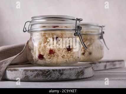 Gläser voll fermentierten Kohl mit roten Preiselbeeren und Leinenserviette auf der Seite. Die Gläser befinden sich auf den Schneidebrettern und auf dem weißen Holztisch. Seitenansicht. H Stockfoto