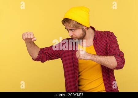 Entschlossener Hipster bärtiger Kerl in Beanie Hut, kariertes Shirt hält geballte Fäuste bereit zum Boxen, Stanzen mit selbstbewussten Ausdruck, kämpfen Stockfoto